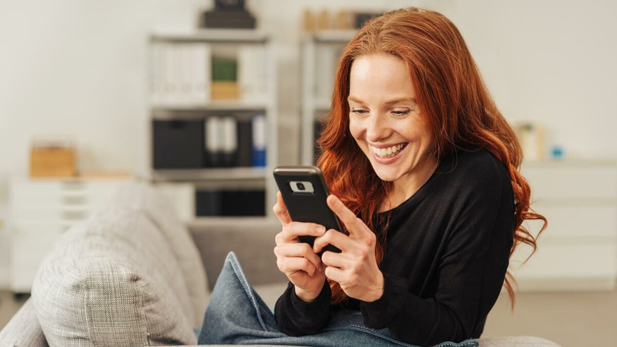 Das Bild zeigt eine lächelnde Frau mit einem Smartphone in der Hand.