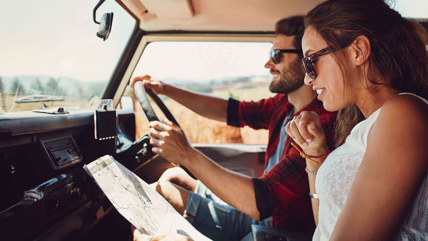 Zwei Personen sind in einem Auto unterwegs: ein Mann fährt, eine Frau hält eine Landkarte in den Händen.