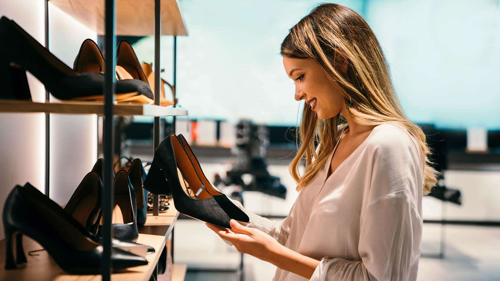 Eine Frau sieht sich schwarze Schuhe in einem Schuhgeschäft an, welches als Bild für personalisierte Shopseiten dient.