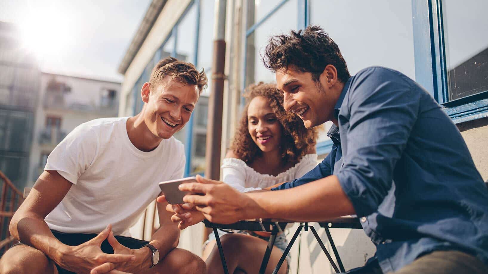 Das Bild zeigt drei Personen, die auf ein Smartphone schauen.